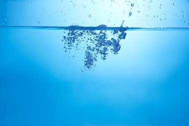 Mavi arka planda su şişesi düşüyor, damlalar düşüyor ve sıçrıyor. Su kabarcıkları dokusu