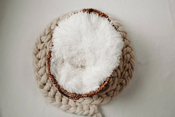 Newborn photography background - woven basket with white faux fur, marcame rug and knitted beige blanket.