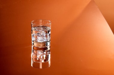 Turuncu arkaplanda buz küpleri olan bir bardak su ve fotokopi alanı