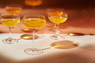 Tarafsız masada uzun gölgeli bakır turuncu içeceklerle dolu üç kokteyl ve kopyalama alanı.