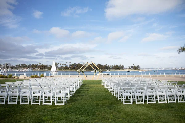 Wedding rhombus double arch with white roses and eucalyptus leaves floral decor. Outdoor city wedding ceremony with bay view and palm trees.