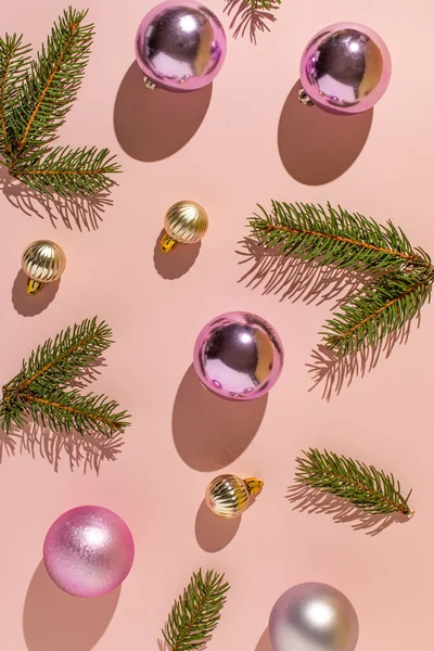 Pembe ve gümüş renkli dekoratif topları ve pastel pembe arka planda köknar dalları olan Noel kompozisyonu. Asgari Yeni Yıl kavramı.