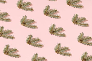 Pastel pembe arka planda yeşil köknar dalları olan modaya uygun bir Noel deseni. Asgari Yeni Yıl duvar kağıdı