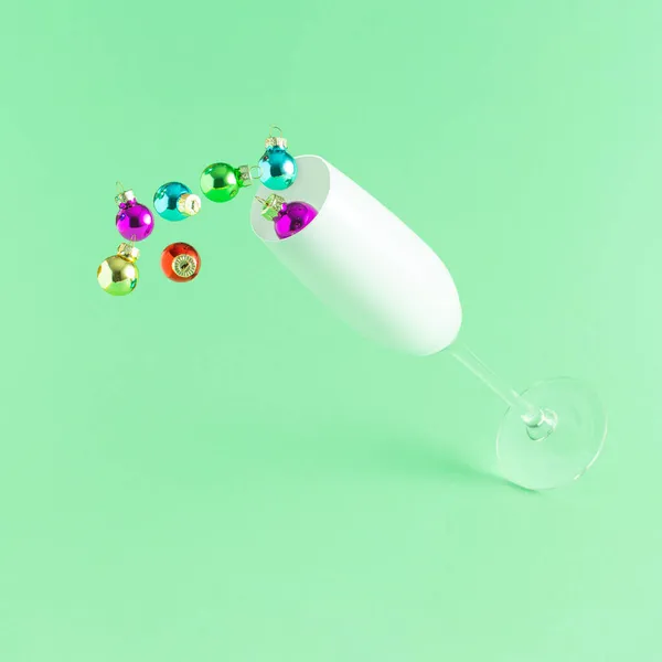 Açık yeşil arka planda rengarenk Noel süslemeleri olan şampanya kadehi, minimum yeni yıl partisi konsepti. Yaratıcı tatil fikri.