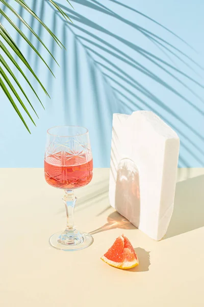 Taze bir kokteyl, bir parça greyfurt, deniz taşı ve yeşil palmiye dallı yaratıcı bir yaz kompozisyonu. Güneşli gün gölgesi. Yaz, tropikal, taze kokteyl konsepti.
