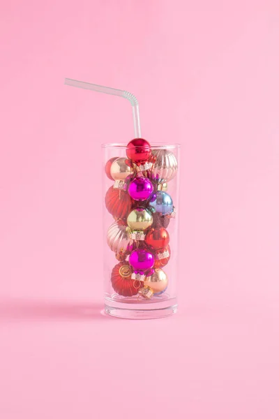 Renkli Noel süsleri olan yaratıcı bir konsept. Pastel pembe arka planda kamışla birlikte bir bardakta. Asgari Yeni Yıl Partisi konsepti