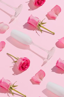 Beyaz şampanya bardakları, güller ve çiçek yapraklarıyla açık pembe arka planda aşk kompozisyonu. Minimum Anneler Günü ya da Sevgililer Günü konsepti.