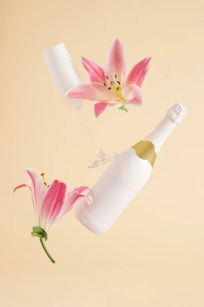 Şampanya şişesi ve pembe çiçekli cam bej arka planda uçuyor. En az Sevgililer Günü ya da Kadın Günü planı. Doğa Partisi konsepti
