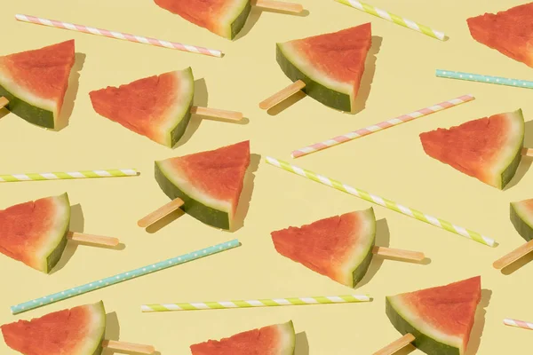 Trendy pattern with fresh watermelon ice cream and colorful straws on a yellow background. Minimal summer party wallpaper.