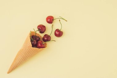 Pastel sarısı arka planda taze kirazlı ve dondurma külahlı moda bir yaz kompozisyonu. Asgari yaz yemeği fikri.