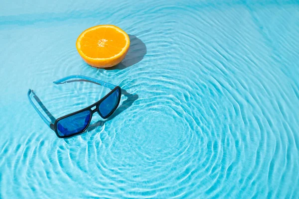 Güneş gözlüklü ve su yüzeyinde bir dilim portakallı son moda bir sahne. Yaz yolculuğu konsepti. Minimum plaj fikri.