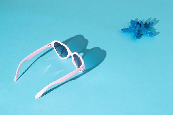 Güneş gözlüklü ve mavi arka planda deniz yıldızlı güneşli bir sahne. Yaz yolculuğu konsepti. Minimum plaj fikri.