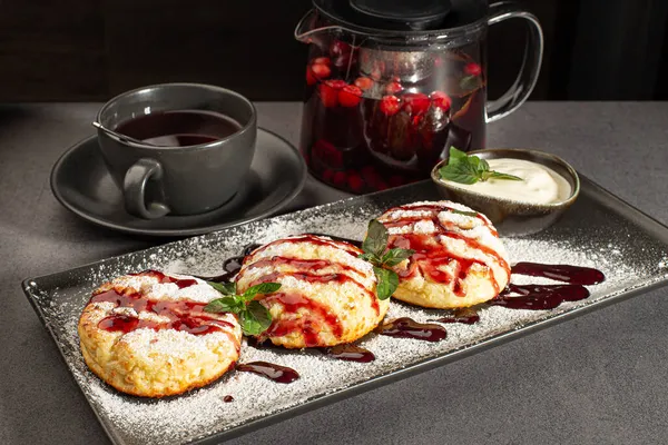 Färskost pannkakor på en mörk bakgrund. Pannkakor med keso på en svart tallrik beströdd med pulversocker. — Stockfoto