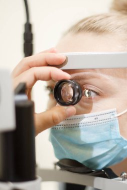 Bir göz doktoru kliniğinde gözleri kontrol eden beyaz bir kadının yakın portresi.