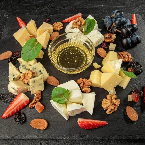 Şarküteri işleme kurulu. Peynirler, böğürtlenler ve bal siyah tahta üzerinde.