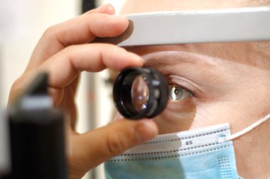 Doktor kadın hastayı büyüteçle kontrol ediyor.