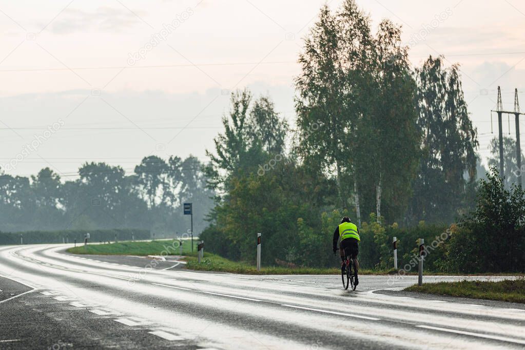 Road cyclist in green west pedaling during in rainy morning time. professional cyclist traveler.