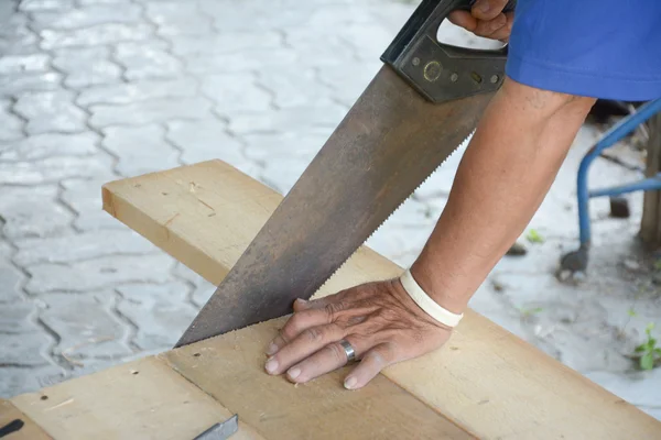 Плотник режет деревянную доску с помощью пилы — стоковое фото