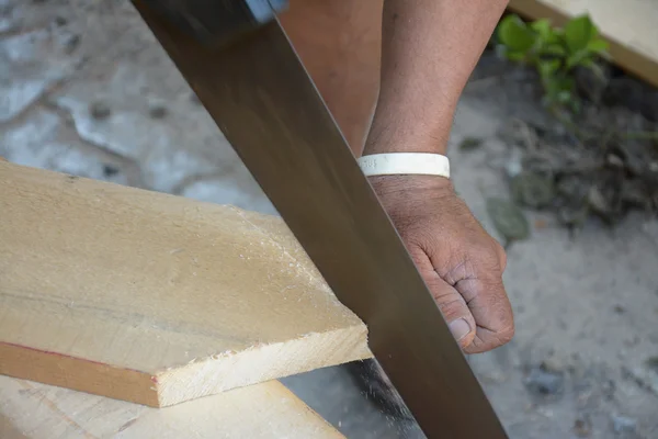 Плотник режет деревянную доску с помощью пилы — стоковое фото
