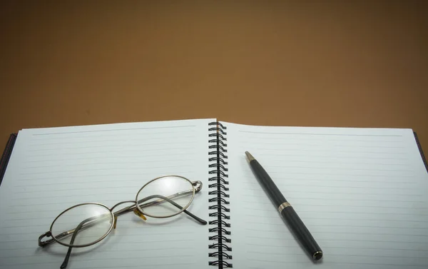 Ноутбук с ручкой и очками на коричневом фоне — стоковое фото