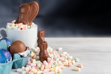 Bahar Paskalya Bayramı 'nın arka planında renkli tatlı şekerleme çikolata gökkuşağı renkli yumurta ve marshmallow yuvasında tavşan kulağı ile doğum festivali sezonu