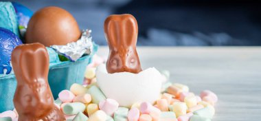 Bahar Paskalya Bayramı 'nın arka planında renkli tatlı şekerleme çikolata gökkuşağı renkli yumurta ve marshmallow yuvasında tavşan kulağı ile doğum festivali sezonu