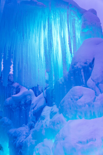 Abstract ice and icicles formations on cold winter night covered in snow and aqua colored lights
