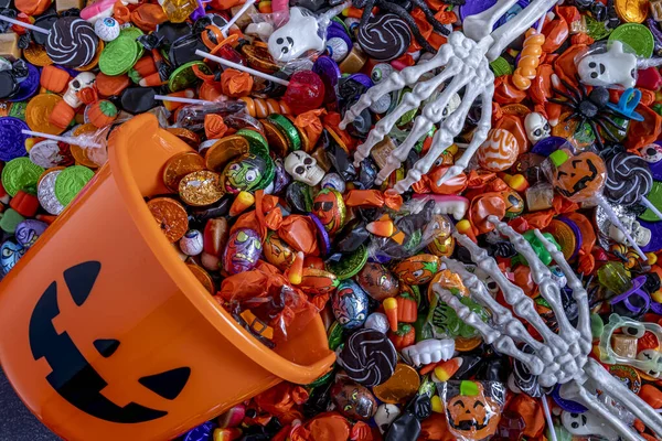 Skeleton Hands Grabbing Variety Halloween Candy Spilling Out Orange Pail — Stock Photo, Image