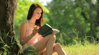 kitap okuma ve bir elma ağacının altında yemek parkta oturan kız