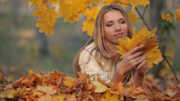 Красивая блондинка лежит на опавших листьях в парке — стоковое видео