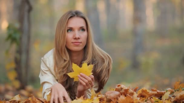 Jolie blonde allongée sur les feuilles tombées dans le parc — Video