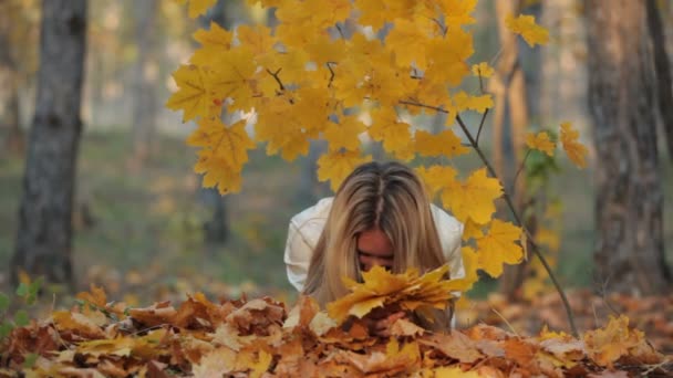 Красивая блондинка лежит на опавших листьях в парке — стоковое видео