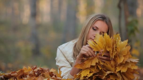 Pretty blonde lying on the fallen leaves in park — Stock Video