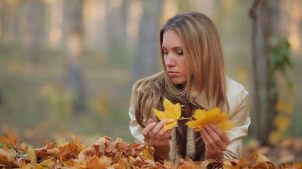 Pretty blonde lying on the fallen leaves in park — Stock Video