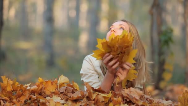 Jolie blonde allongée sur les feuilles tombées dans le parc — Video