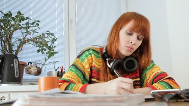 Menina bonita está ouvindo música em fones de ouvido enquanto estuda . — Vídeo de Stock