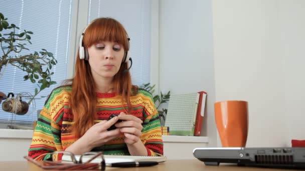 Menina bonita está ouvindo música em fones de ouvido enquanto estuda . — Vídeo de Stock