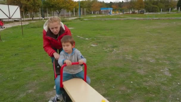 Dwie osoby dorosłe, kołysanie chłopczyk na plac zabaw dla dzieci. — Wideo stockowe