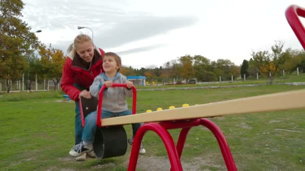 Дівчинка розмахує маленьким хлопчиком на дитячому майданчику — стокове відео