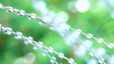 Gün batımında dikenli tellerle çevrili 4K uzun hapishane çiti, güneş uzak tel örgülerin arasından batıyor.