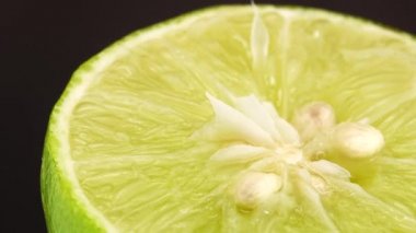 Yeşil limonun 4K dönüşü. Üst görünüm, 360 derece döndürme, siyah arkaplanda izole edilmiş bir kesikte limonun yakın çekimi