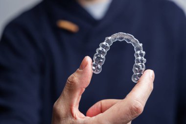 Man holding one transparent aligner. Invisalign orthodontics concept clipart