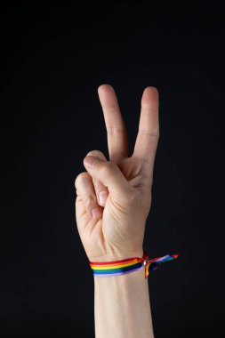 Hand with LGBT pride rainbow wristband making victory sign. Black background