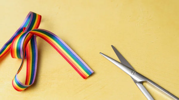 LGBT rainbow ribbon ready to be cut. Yellow background