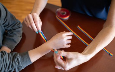 Genç bir kızın bileğine LGBT bilekliği takan bir kadın.