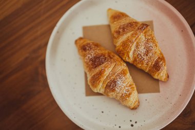 Bir tabakta iki iştah açıcı kruvasan kafedeki ahşap bir masaya konur..