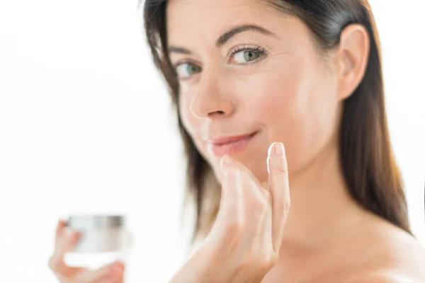 Mujer de unos cuarenta años aplicando crema facial —  Fotos de Stock