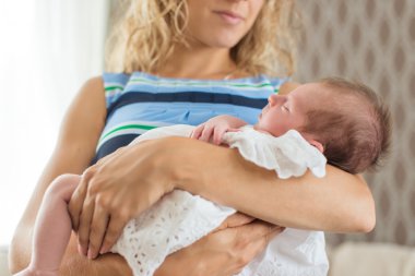 Annesinin kollarında bir elbise giyen kız bebek