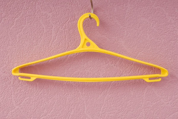 Yellow plastic coat-hanger is on lilac wall — Stock Photo, Image