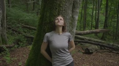 30 'lu yılların bayan turisti yürüyüş yapmaktan ve ağaçta yosun tutmaktan yoruldu. Kadın ağaca yaslanıyor ve dinleniyor. Doğaya bakıyor.. 